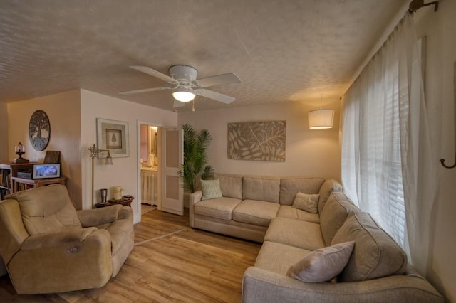 living room with a textured ceiling, ceiling fan, and light wood-type flooring