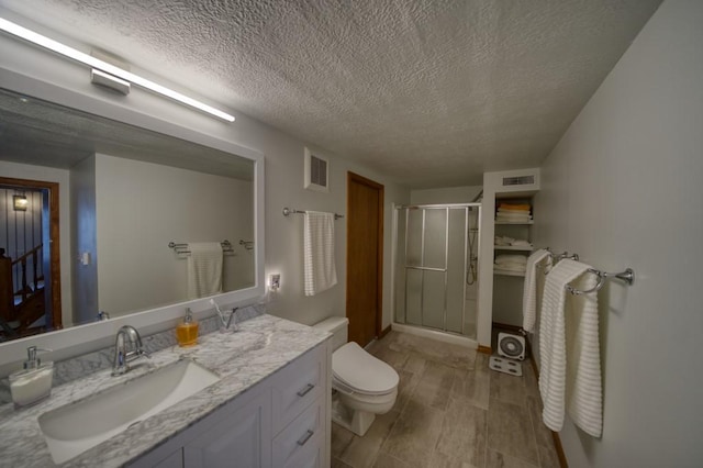 bathroom with vanity, a textured ceiling, a shower with shower door, and toilet