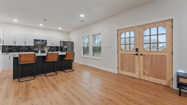 kitchen featuring a kitchen breakfast bar, a center island, light hardwood / wood-style floors, black appliances, and white cabinets