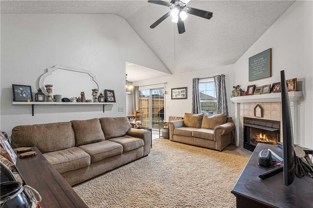 living room with a tile fireplace, ceiling fan, carpet, a textured ceiling, and vaulted ceiling