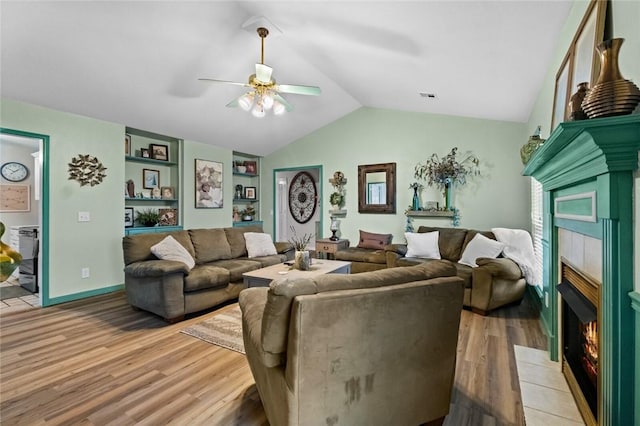 living room featuring hardwood / wood-style flooring, vaulted ceiling, a tile fireplace, and ceiling fan