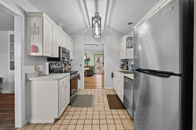 kitchen featuring appliances with stainless steel finishes, sink, white cabinets, hanging light fixtures, and light tile patterned floors