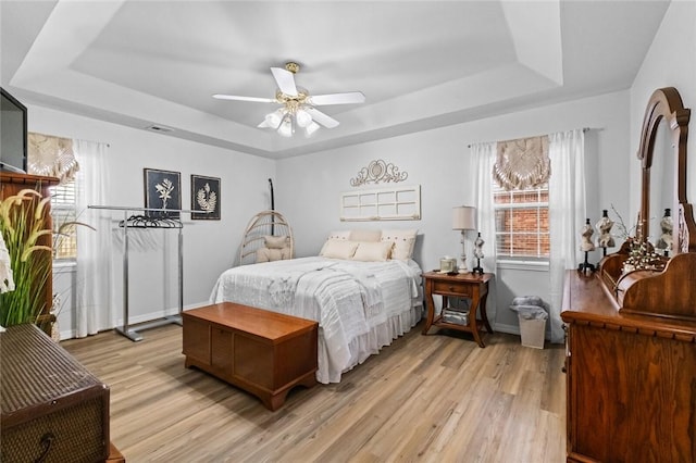 bedroom featuring a tray ceiling, light hardwood / wood-style floors, and multiple windows