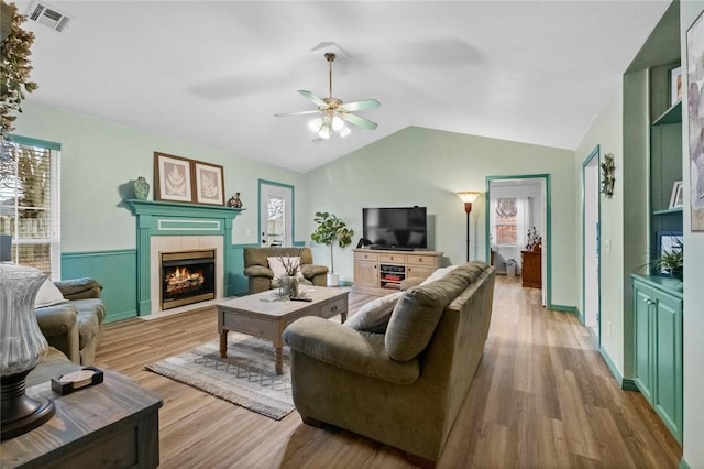 living room with lofted ceiling, light hardwood / wood-style floors, a tile fireplace, and ceiling fan