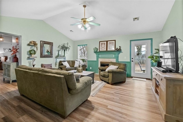 living room featuring plenty of natural light, a tiled fireplace, vaulted ceiling, and light wood-type flooring