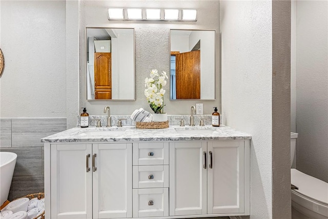 full bathroom with double vanity, toilet, a sink, and a textured wall