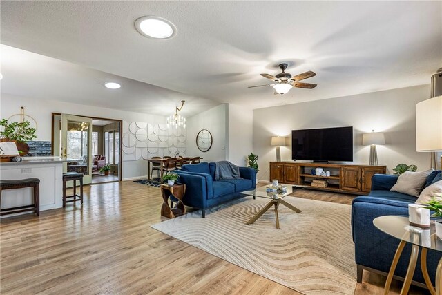 living room featuring ceiling fan with notable chandelier and light wood-type flooring