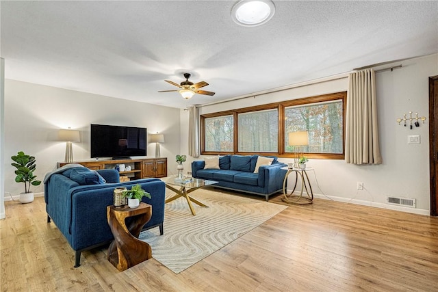 living room with ceiling fan, a textured ceiling, and light wood-type flooring