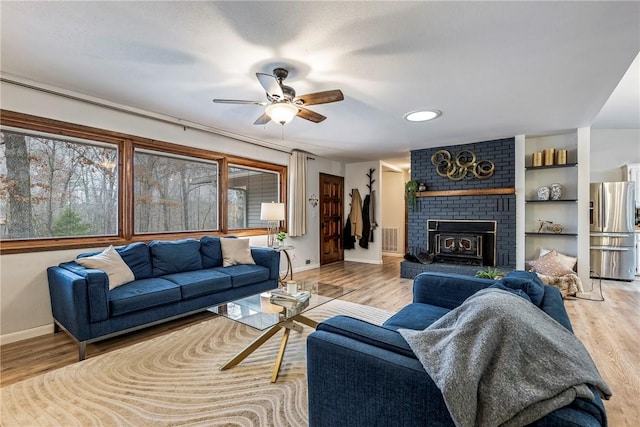 living room featuring ceiling fan, a brick fireplace, and light wood-type flooring