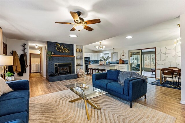 living room featuring light hardwood / wood-style floors, a brick fireplace, washer / clothes dryer, ceiling fan with notable chandelier, and vaulted ceiling