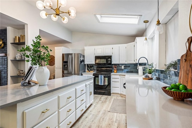 kitchen featuring vaulted ceiling, decorative light fixtures, white cabinets, light hardwood / wood-style floors, and black appliances