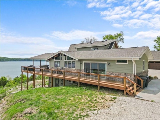 rear view of property with a garage, a deck with water view, and a lawn