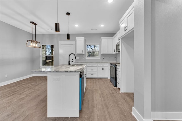 kitchen with light wood finished floors, stainless steel appliances, an island with sink, and a sink