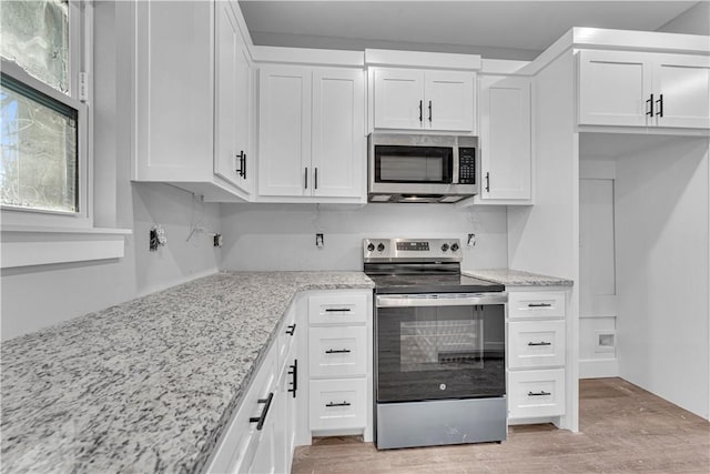 kitchen featuring white cabinets, stainless steel appliances, light wood-style floors, and light stone countertops