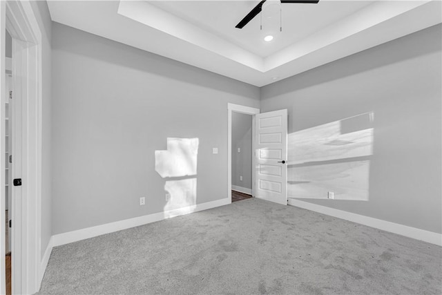unfurnished bedroom featuring ceiling fan, a raised ceiling, baseboards, and carpet floors