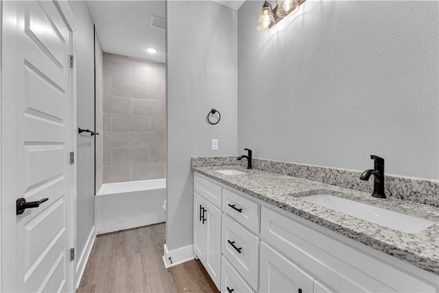 full bath featuring double vanity, wood finished floors, baseboards, and a sink