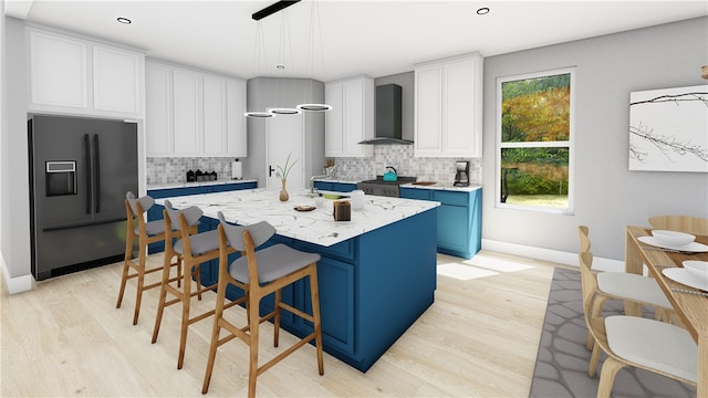 kitchen featuring white cabinetry, decorative light fixtures, black refrigerator with ice dispenser, a center island with sink, and wall chimney range hood