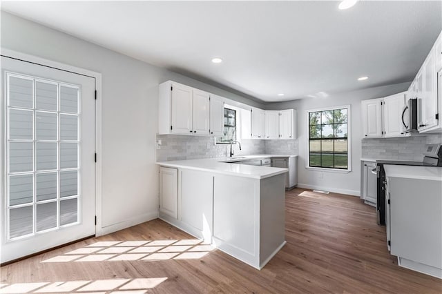 kitchen with sink, light hardwood / wood-style flooring, kitchen peninsula, stainless steel appliances, and white cabinets