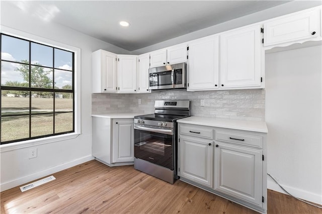 kitchen with white cabinetry, backsplash, light hardwood / wood-style flooring, and appliances with stainless steel finishes