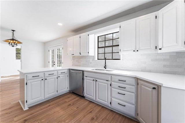 kitchen with sink, hardwood / wood-style flooring, dishwasher, white cabinetry, and kitchen peninsula