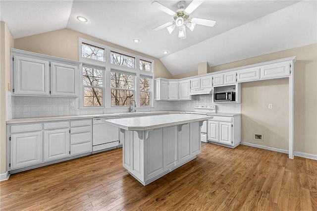 kitchen featuring lofted ceiling, white appliances, a center island, and white cabinets