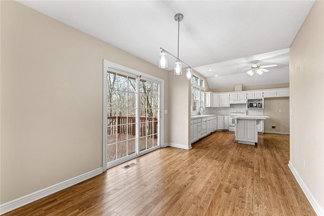 kitchen with electric stove, sink, pendant lighting, white cabinetry, and a center island