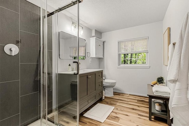 bathroom featuring a shower with shower door, wood-type flooring, vanity, toilet, and a textured ceiling