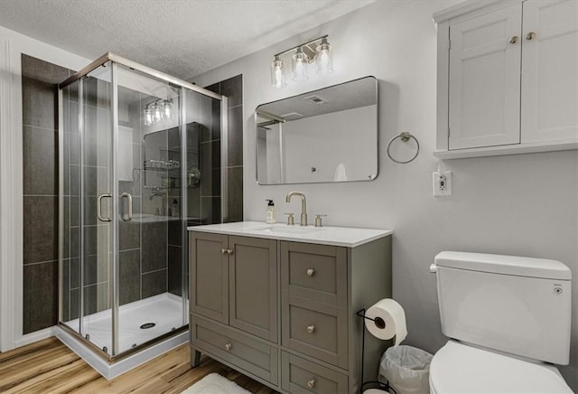 bathroom with hardwood / wood-style floors, vanity, a textured ceiling, a shower with shower door, and toilet