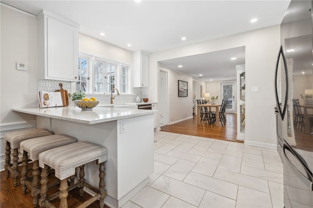 kitchen with a breakfast bar, white cabinetry, light stone counters, stainless steel refrigerator, and kitchen peninsula