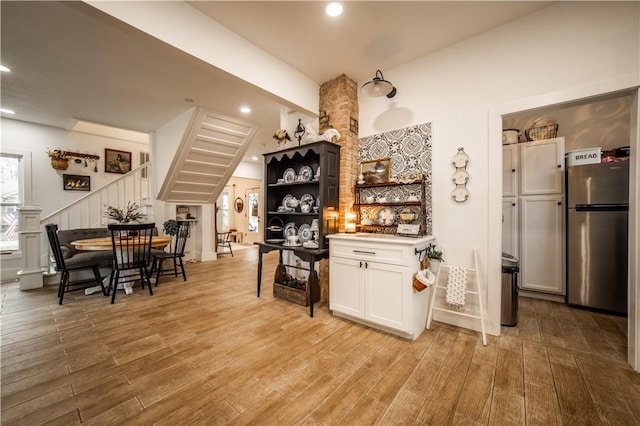 bar with light hardwood / wood-style flooring, stainless steel fridge, and white cabinets