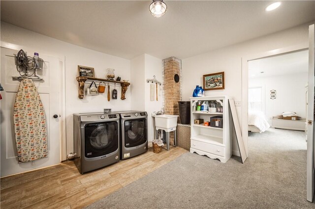 clothes washing area with recessed lighting, laundry area, washer and dryer, a sink, and wood finished floors
