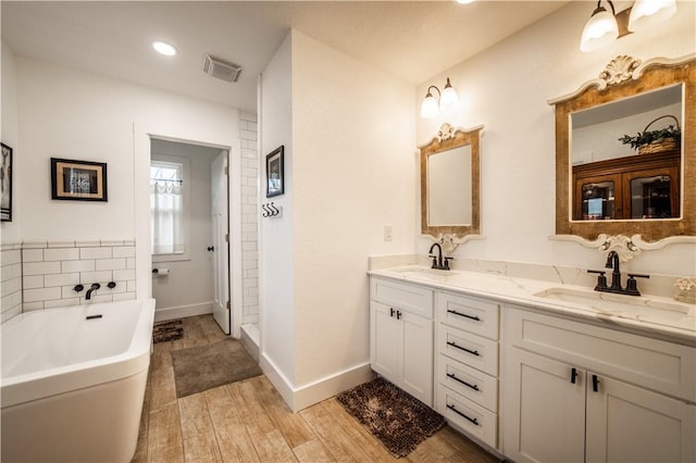 bathroom featuring a freestanding tub, double vanity, a sink, and visible vents