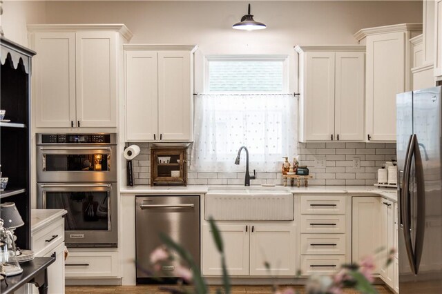 kitchen with a sink, backsplash, appliances with stainless steel finishes, and white cabinetry