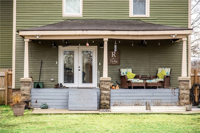 view of exterior entry with french doors, a shingled roof, fence, and a yard