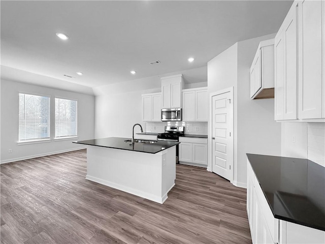 kitchen with sink, a kitchen island with sink, stainless steel appliances, white cabinets, and decorative backsplash