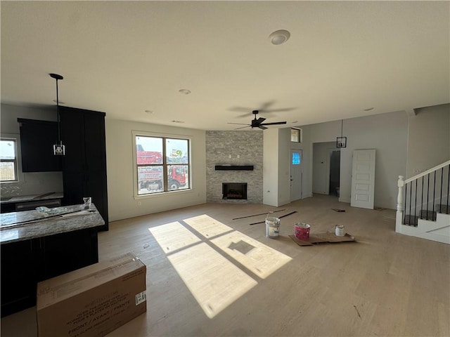 unfurnished living room featuring a fireplace, a healthy amount of sunlight, stairs, and ceiling fan