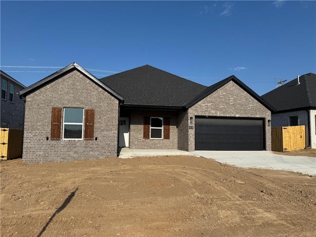 view of front of property featuring brick siding, fence, driveway, and a garage