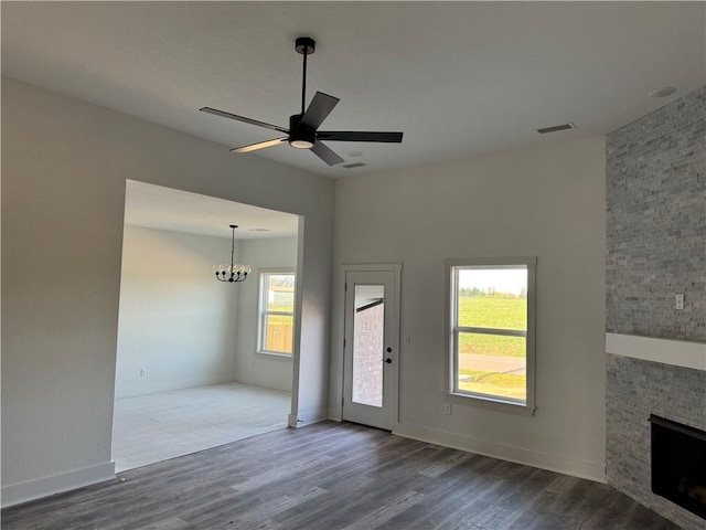 unfurnished living room featuring baseboards, visible vents, ceiling fan with notable chandelier, wood finished floors, and a fireplace