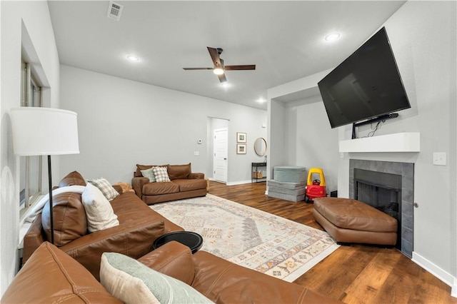 living room featuring a tile fireplace, wood-type flooring, and ceiling fan