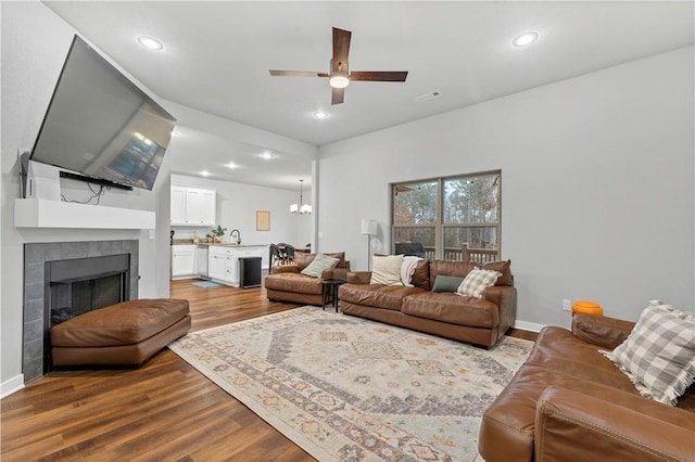 living room featuring ceiling fan with notable chandelier, a fireplace, sink, and light hardwood / wood-style flooring