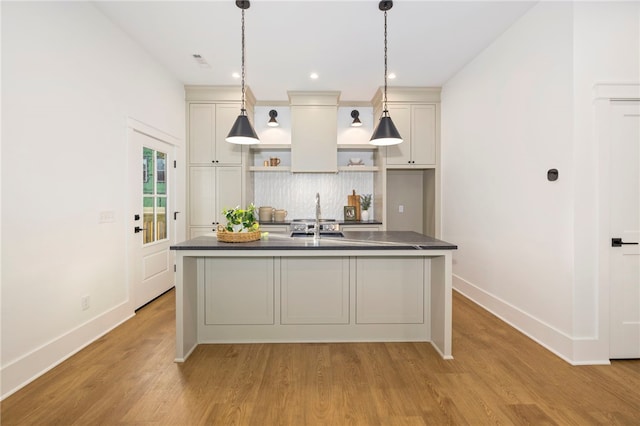 kitchen featuring a kitchen island with sink, backsplash, decorative light fixtures, and light wood-type flooring