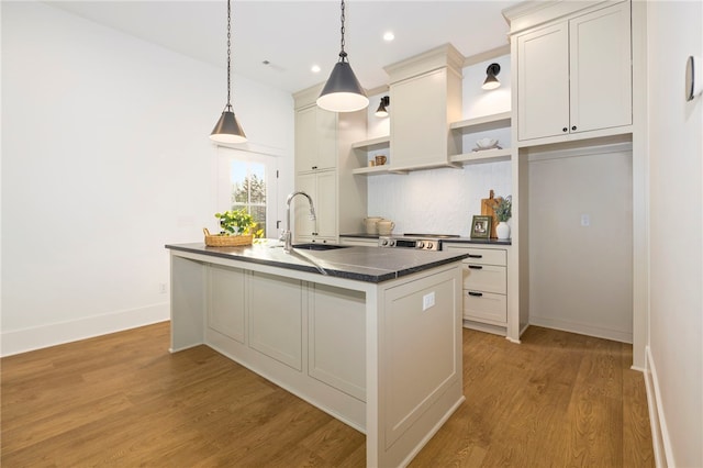 kitchen featuring pendant lighting, tasteful backsplash, sink, a kitchen island with sink, and light hardwood / wood-style flooring