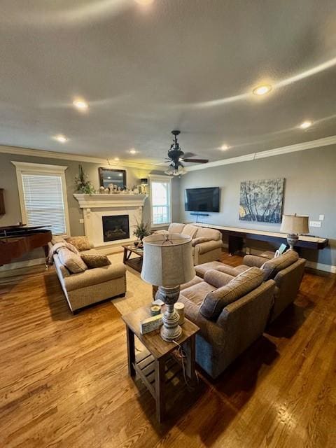 living room with crown molding, a fireplace, recessed lighting, a ceiling fan, and wood finished floors