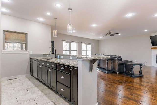 kitchen with a kitchen bar, sink, light stone counters, decorative light fixtures, and a tile fireplace