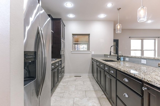 kitchen featuring sink, appliances with stainless steel finishes, light stone countertops, light tile patterned flooring, and decorative light fixtures