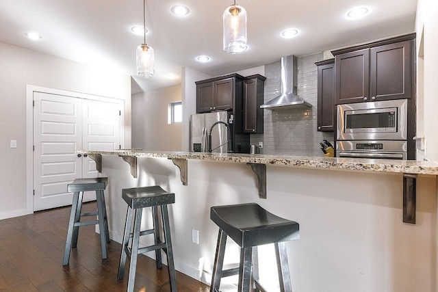 kitchen featuring pendant lighting, stainless steel appliances, a breakfast bar area, and wall chimney range hood