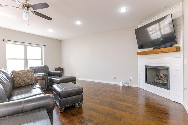 living room featuring dark wood-type flooring, a large fireplace, and ceiling fan