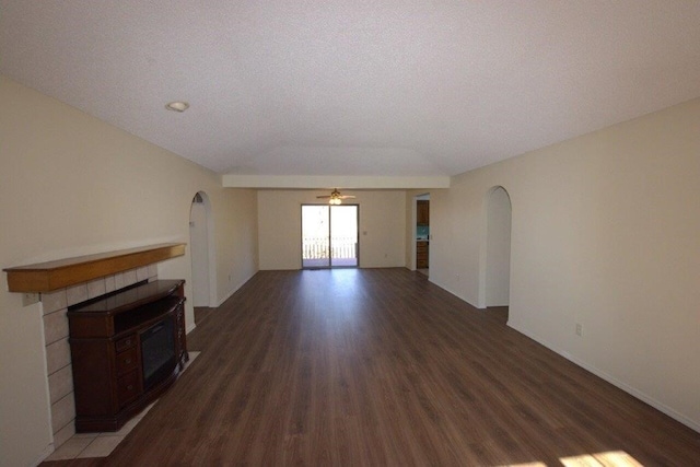 unfurnished living room with lofted ceiling, dark wood-type flooring, a tile fireplace, and ceiling fan