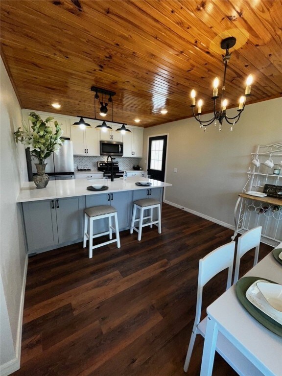 kitchen with decorative backsplash, a chandelier, appliances with stainless steel finishes, a breakfast bar area, and dark wood-style floors