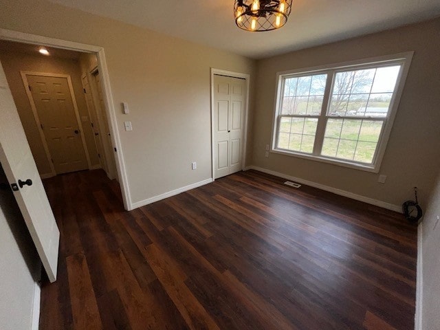 unfurnished bedroom featuring a closet, visible vents, a chandelier, baseboards, and dark wood finished floors